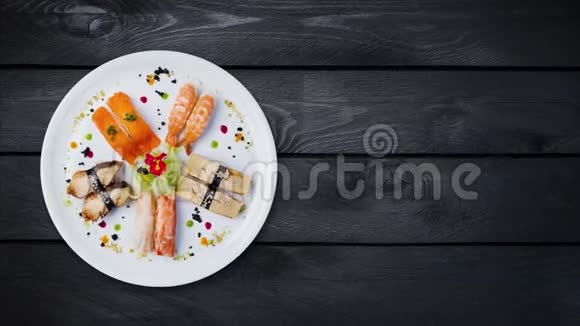 旋转生鱼片设置在白色的圆形盘子上装饰有小花日本菜俯视黑色木制视频的预览图