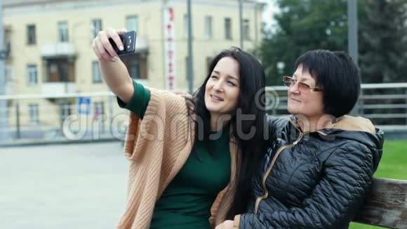 妈妈和女儿正在一起玩同时在智能手机上做自拍一位成年妇女在一个年轻人身上画角视频的预览图
