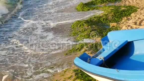一艘空的蓝白相间的渔船在海岸上那是暴风雨后抛出的绿藻有泡沫的波浪视频的预览图