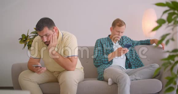 两位白种人使用手机坐在舒适的室内沙发上的特写镜头视频的预览图