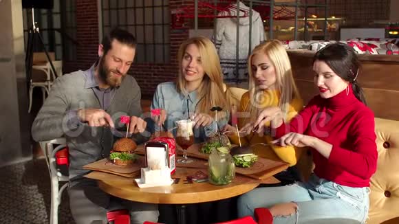 一群嬉皮士用刀叉从黑面包中吃掉漂亮的汉堡视频的预览图