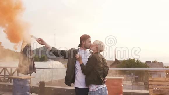 帅哥和他快乐的女友浪漫地接吻英俊的年轻人举着彩色的烟吻他视频的预览图