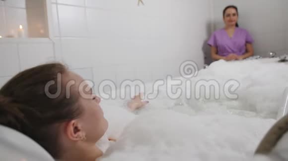 女人控制水疗按摩浴缸做按摩客户躺在浴缸里女性操作员通过视频的预览图