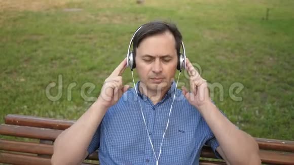 一个英俊的年轻人在公园里休息带着耳机听智能手机里的音乐在外面跳舞视频的预览图