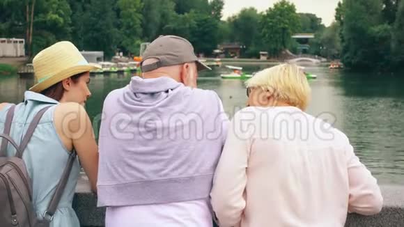 快乐的家庭享受假期老年人和他们的未成年女儿站在湖边公园观光视频的预览图