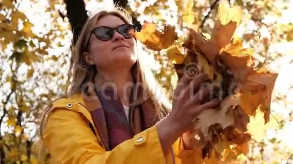 穿着黄色雨衣的年轻金发女子竟然不肯在公园里扔秋叶视频的预览图