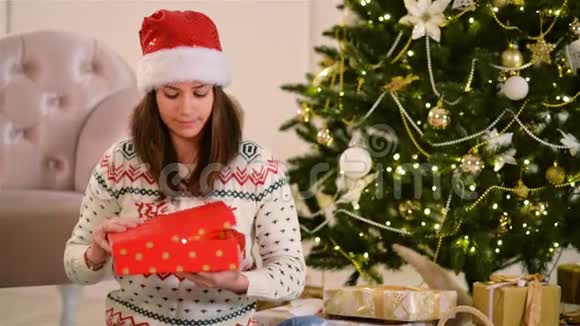 圣诞帽中的女性肖像正在打开礼物盒圣诞树在背景上新年快乐理念视频的预览图