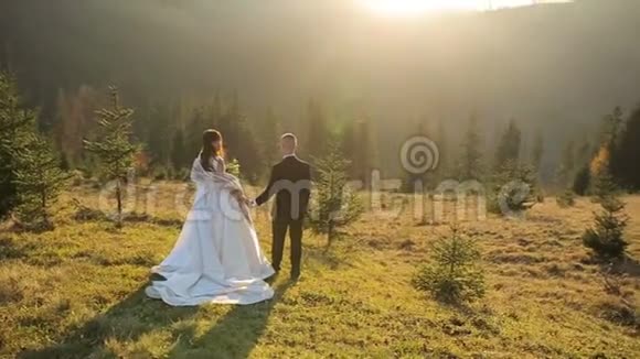 夕阳西下年轻而美丽的新婚夫妇一起在山上的斜坡上可爱的新郎和新娘风视频的预览图
