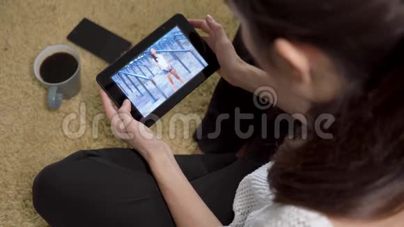 女孩在地毯上坐在家中用平板电脑屏幕观看体育训练视频视频的预览图