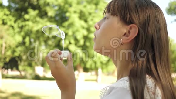 小女孩在公园里玩吹泡泡特写慢动作美丽的女孩在吹肥皂泡视频的预览图