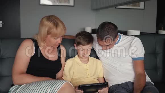 幸福的家庭沙发上有一块平板电脑父母带着一个孩子连接到一个数字平板电脑视频的预览图
