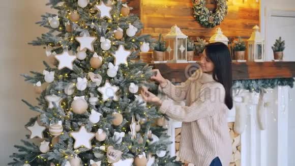 微笑的年轻女士正在用球星星和灯光装饰圣诞树并享受节日的快乐视频的预览图