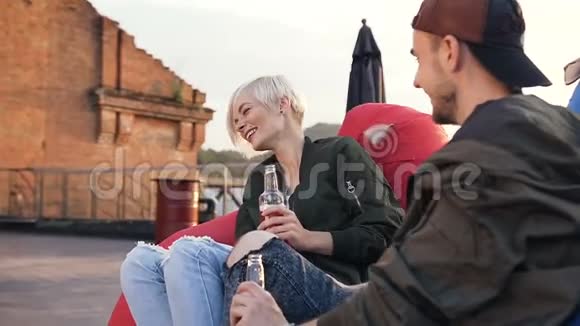年轻人和女孩坐在露台咖啡馆的多色扶手椅上喝能量饮料两个朋友玩得开心视频的预览图