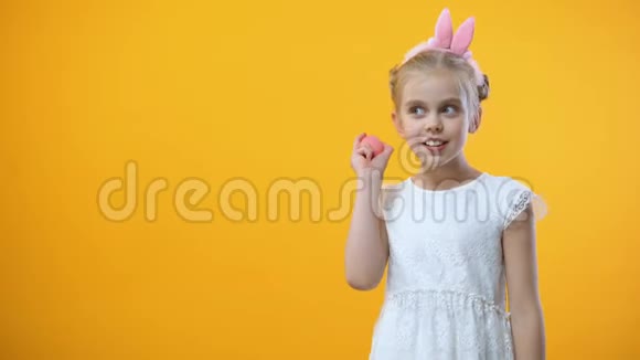 穿着白色连衣裙的可爱女孩在黄色背景上摇动着彩色粉红色的鸡蛋节日视频的预览图