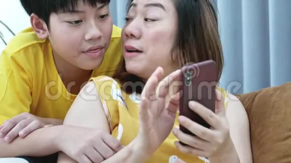 幸福的家庭母亲和她的儿子带着智能手机看电视微笑着放松生活方式的概念慢动作视频的预览图