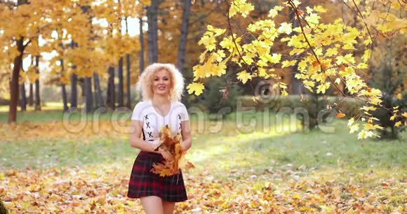 快乐的金发女人穿着性感的作物上衣和裙子在公园里玩树叶视频的预览图