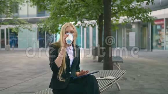 年轻的商业女性使用平板电脑和喝咖啡现代行政女性西装革履坐在长椅上户外冲浪视频的预览图