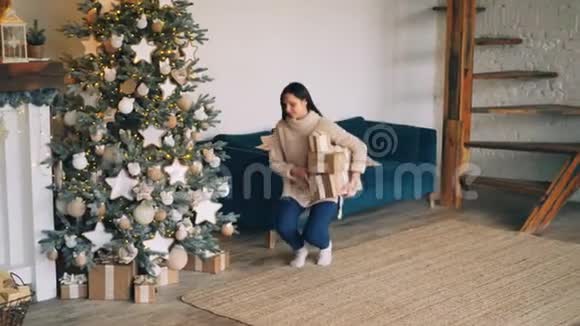 年轻女子正把礼物盒带到圣诞树下放在圣诞树下然后看礼物和礼物视频的预览图