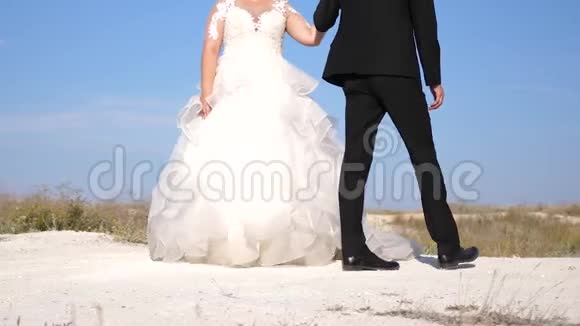 穿西装的新郎和穿白裙子的新娘华尔兹浪漫的男人和女人在白色海滩上的蓝天上跳舞视频的预览图