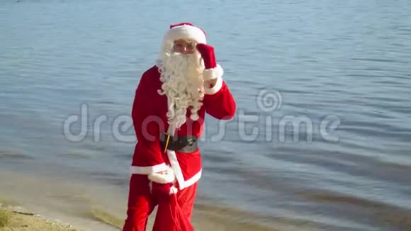 圣诞老人拿着一袋礼物站在河边或湖边视频的预览图