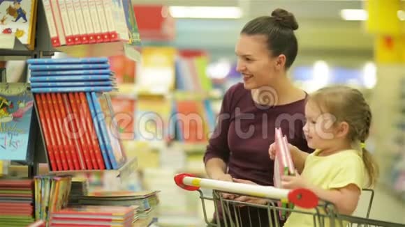 在超市里微笑的母亲和女儿女儿帮助母亲选择一本书可爱的女儿坐在里面视频的预览图