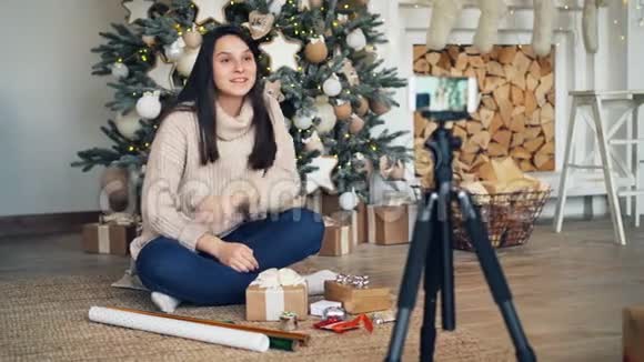 聪明的女孩创意vlogger正在录制关于礼品盒和礼物包装的视频坐在装饰的圣诞节附近视频的预览图
