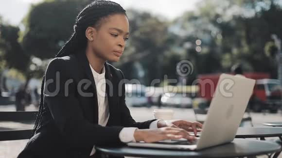 一位非洲裔美国青年妇女坐在夏季露台的咖啡馆里在笔记本电脑上工作商务工作视频的预览图