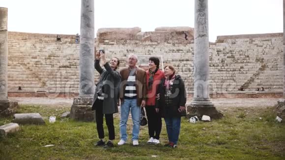 微笑的年轻欧洲女孩和快乐的高级旅游团体自拍附近的旧圆形剧场废墟意大利奥斯蒂亚视频的预览图
