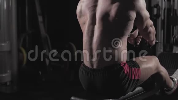 在黑暗健身房的健身机器上用慢动作的烟雾进行男人健身的特写视频的预览图
