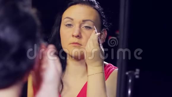 一个年轻的黑发女人穿着一件红色的裙子在镜子前在她的眼皮上投下明亮的阴影视频的预览图