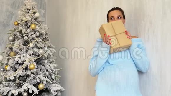 怀了孕的妈妈拿着白色圣诞礼物站在圣诞树旁视频的预览图