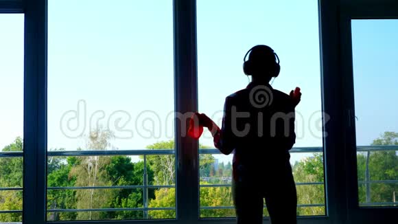 深色轮廓戴手套的女人的影子戴耳机用清洁剂喷洒清洁产品清洁窗户视频的预览图