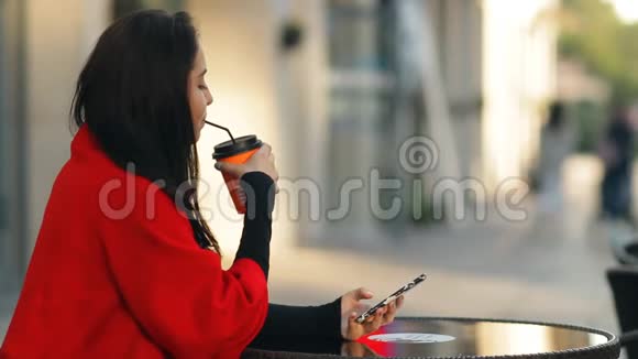 时尚迷人的女人喝咖啡使用智能手机坐在桌子上的咖啡馆在街上视频的预览图
