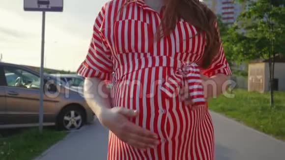 孕妇腹部特写怀孕的女孩在夏天抚摸她的大肚子在城市里散步中等视频的预览图
