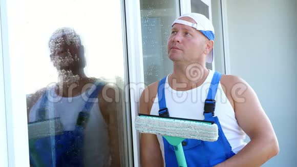 特写一位男清洁工人的肖像穿着蓝色工作服戴着一顶帽子戴着一个专门的拖把视频的预览图