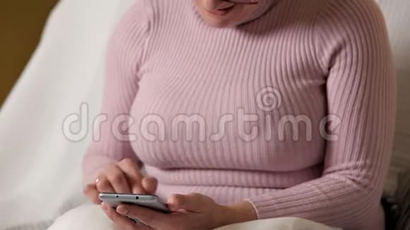 一个穿着粉色夹克戴眼镜的女人坐在白色沙发上发短信视频的预览图