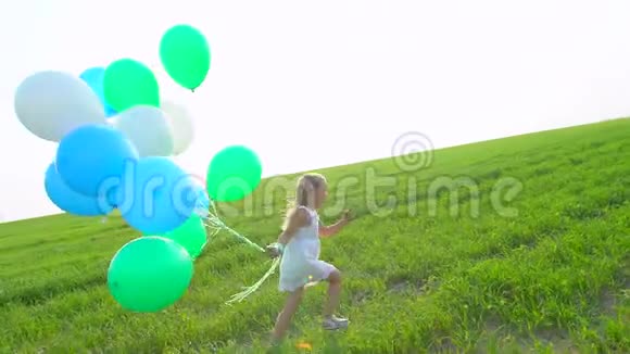 穿着裙子的小女孩手里拿着气球穿过绿色的麦田孩子孩子在花园里跑视频的预览图