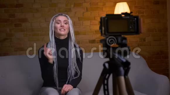 一位年轻有魅力的女性博客写手在沙发上坐着镜头直播视频的预览图