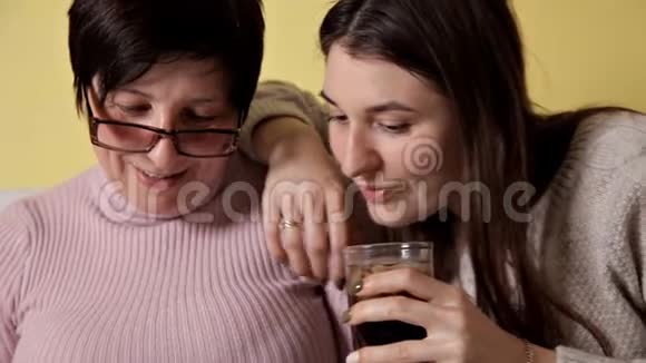 母女俩坐在家里的沙发上智能手机的使用浏览阅读新闻喝可口可乐视频的预览图