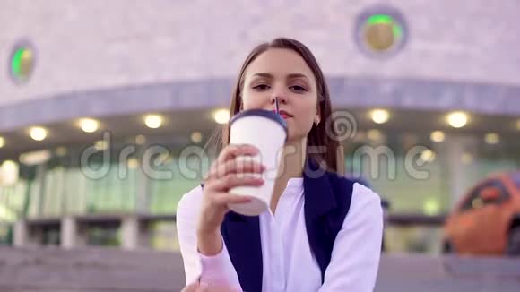 美丽的女孩喝着咖啡在晚上的城市的街道上看着相机特写视频的预览图