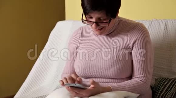 一个穿着粉色夹克戴眼镜的女人坐在白色沙发上发短信视频的预览图