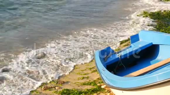 一艘空的蓝白相间的小船在海岸上暴风雨过后它们是绿藻带泡沫节拍的波浪视频的预览图