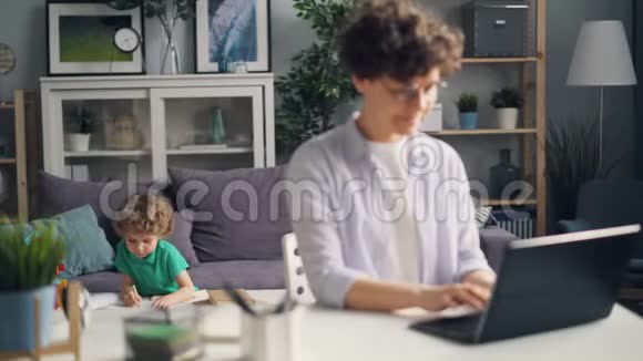 小孩子在画画而母亲是一个自由职业者在桌上用手提电脑打字视频的预览图