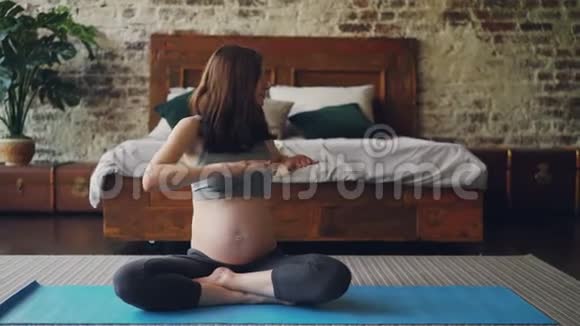 适合怀孕的女孩做运动坐在卧室地板上的瑜伽垫上左右转动身体视频的预览图