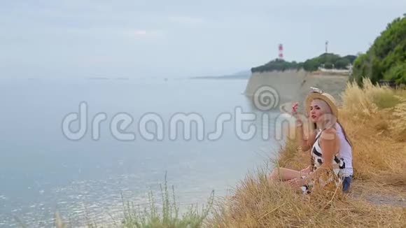 可爱积极的金发女孩和黑发女孩坐在悬崖边微笑着看着无边的蓝色大海视频的预览图