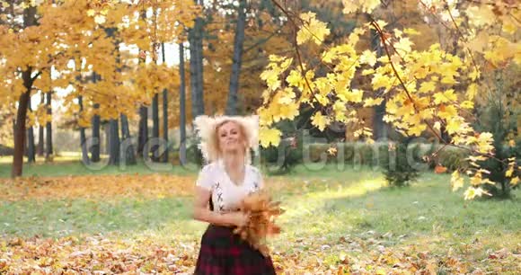 快乐的金发女人穿着性感的作物上衣和裙子在公园里玩树叶视频的预览图
