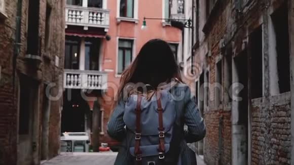 镜头跟随年轻的女游客背着背包在美丽的黑暗古城街道上漫步威尼斯慢动作视频的预览图
