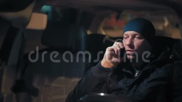 特写镜头男人在电话上说话晚上坐在停车场的车轮上视频的预览图