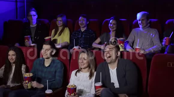 年轻的朋友坐在电影院里喝着爆米花和饮料看一部喜剧电影视频的预览图