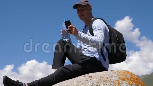 男性旅行者在使用电话和石头休息时喝水视频的预览图